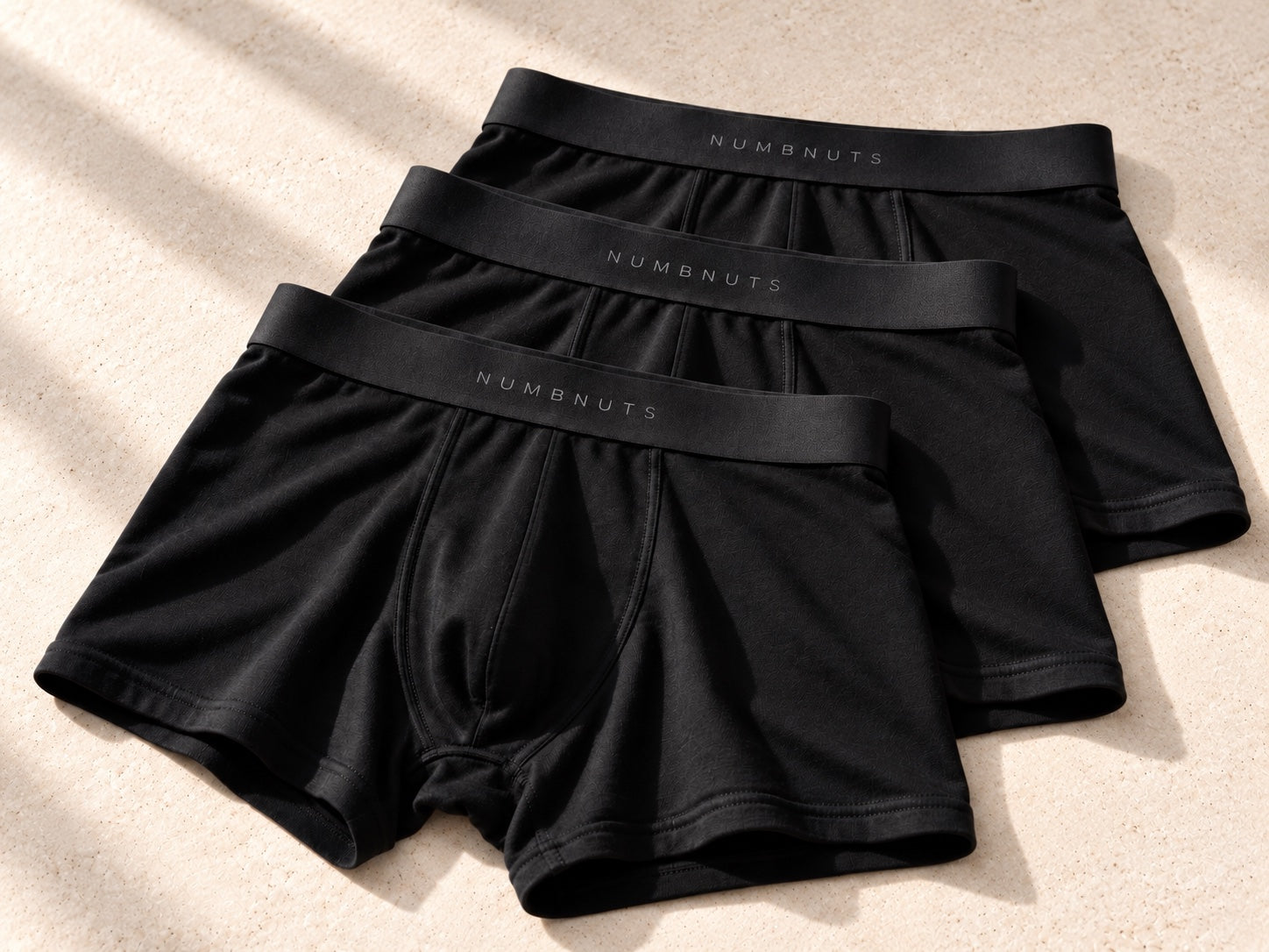 Product visualisation of three black NUMBNUTS merino-body boxers with separate branded waistbands and no inserts
